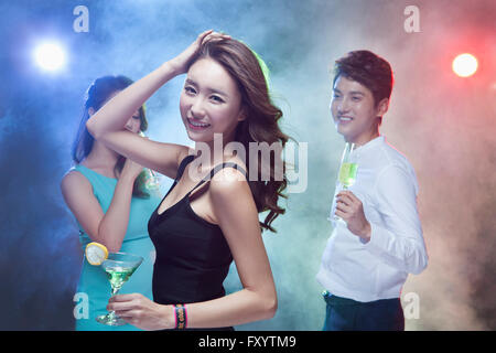 Portrait of young smiling woman holding cocktail glass with her friends at nightclub Stock Photo