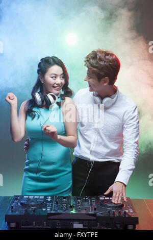 Two young smiling DJ couple dancing and playing music face to face at nightclub Stock Photo
