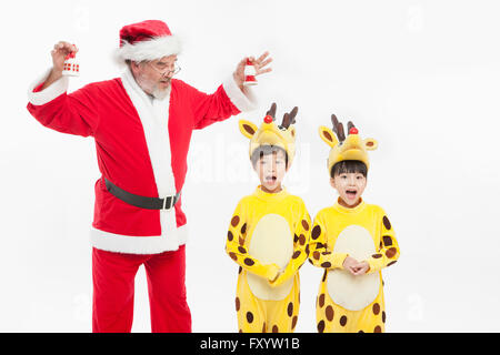 Smiling Santa Claus ringing bells, boy and gril dressed like deer singing staring at front Stock Photo