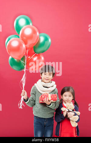 Korean boy and girl holding balloons, present box and a teddy bear staring at front with smiles Stock Photo