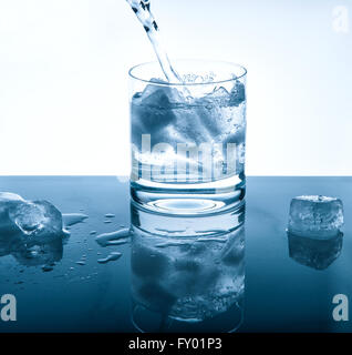 Water cold drink pouring into glass over bright background. Blue colored picture