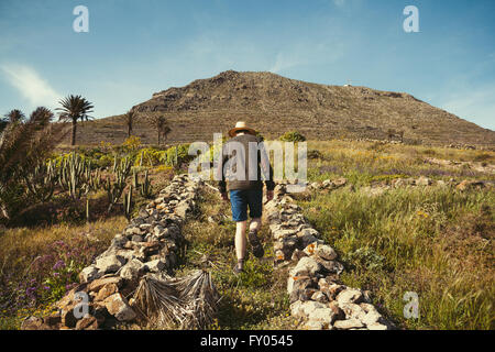Young man walking towards a mountain wearing casual clothes and a straw hat in Lanzarote, Canary Islands. Stock Photo