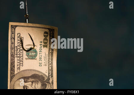 Half of a $100 bill hanging on a fishing hook with light blue background Stock Photo