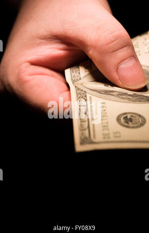A man's right hand emerging from the shadows holding out a $100 bill