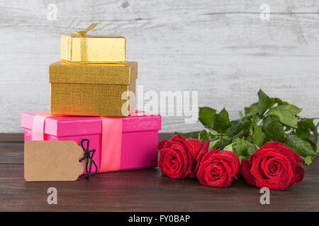 Three red roses and three gift boxes with empty tag on wooden table with copy space Stock Photo