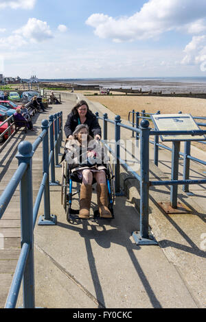An elderly lady is pushed up a concrete ramp in a wheelchair by her carer or assistant on a sunny day in Whitstable.  MODEL RELEASED. Stock Photo