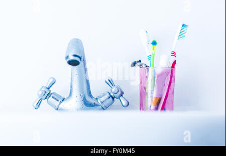 Plastic glass with toothbrushes on basin near water tap Stock Photo