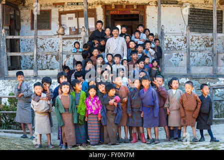 Children and principal wearing traditional dress standing on steps of dilapidated primary school in Nimshong vilage, Bhutan Stock Photo