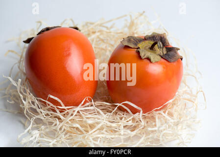 Two orange persimmons on a white table with straw Stock Photo