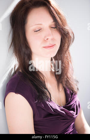 Woman sitting with eyes closed. Lifestyle image of young woman showing relaxation, contemplation and contentment. Stock Photo