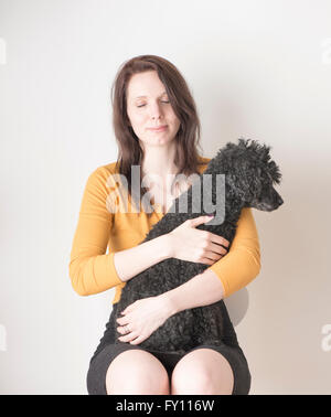 Woman with eyes closed holding black poodle in her arms. Lifestyle image showing affection and the bond between dog and human. Stock Photo