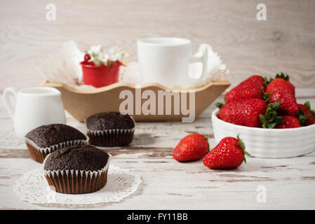 Chocolate muffins, coffee, strawberries, a vase of white flowers. Light wood rustic background Stock Photo