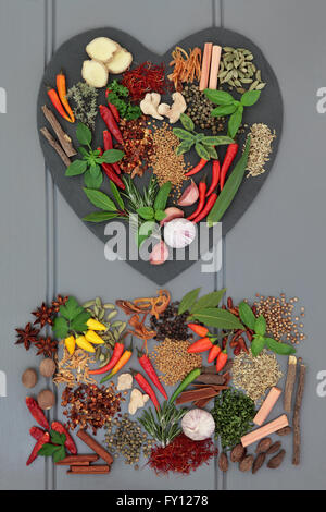 Herb and spice ingredients on heart shaped slate and loose over grey wooden background. Stock Photo