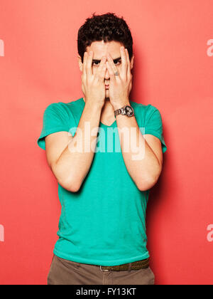 Portrait of young man covering face with hands against red background Stock Photo
