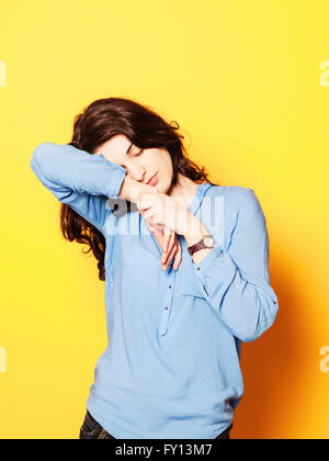 Tired young woman sleeping on hand against yellow background Stock Photo