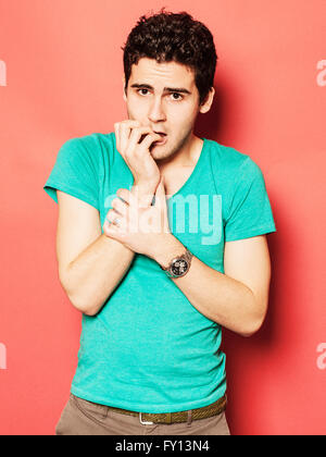 Portrait of nervous young man biting nails against red background Stock Photo