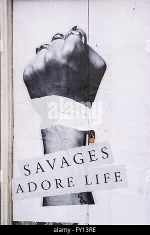 Billboard on an old white door showing a man's fist with silver rings and the words 'Savages adore life' below Stock Photo