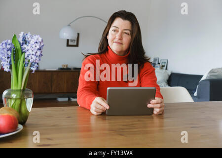 Mature woman looking away while holding digital tablet on table at home Stock Photo