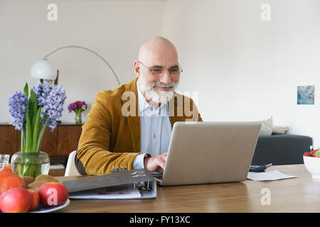 Smiling mature man using laptop on table at home Stock Photo