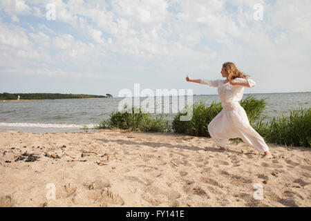 Young woman practicing yoga on sea shore at beach against sky Stock Photo