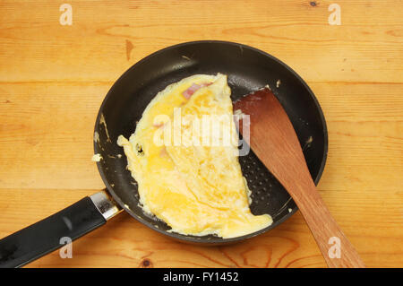 Cheese and ham omelette in a frying pan with a wooden spatula on a kitchen worktop Stock Photo