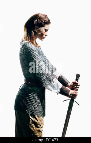Side view of woman wearing chain mail with sword standing against white background Stock Photo