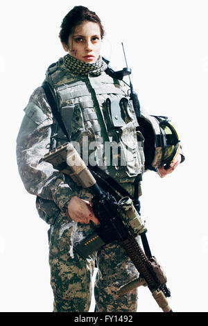 Female soldier holding rifle and helmet while standing against white background Stock Photo