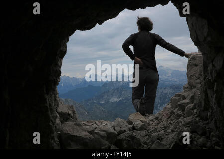 Rear view of woman standing on rock against mountains seen through cave Stock Photo