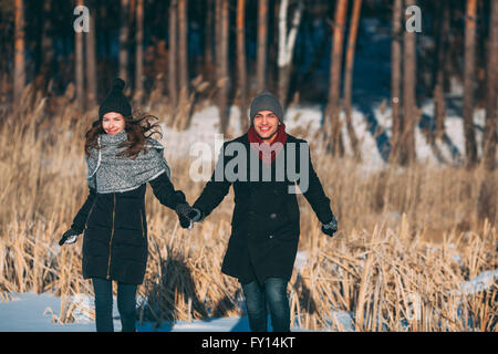 Happy couple holding hands while walking on snow covered field Stock Photo