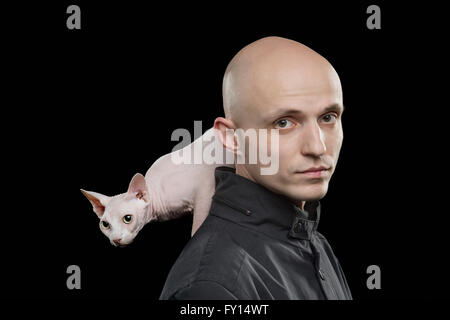 Portrait of bald man carrying Sphynx hairless cat on shoulder against black background Stock Photo