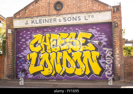 Street art mural on the garage door of an old brick building with "Cheese London" in bright yellow letters Stock Photo