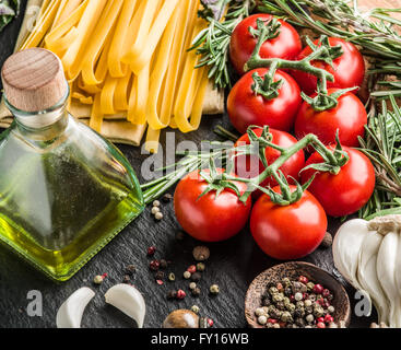 Pasta ingredients. Cherry-tomatoes, spaghetti pasta, rosemary and spices on a graphite board. Stock Photo