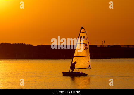 Yachtsman sailing dingy at sunset on Marine Lake. Southport, Marine Lake, Merseyside 20th April, 2016. UK Weather. Light Winds and a Golden Sunset over Marine Lake as 504 Ted James from Southport Sailing Club sails his RS Vareo yacht. The boat is a spinnaker powered single-hander. The stable hull, responsive rig and easy handling systems make the RS Vareo an attainable challenge in the right conditions- but not today. Stock Photo