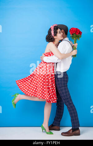 Young smiling couple in retro style standing hugging each other with red roses Stock Photo