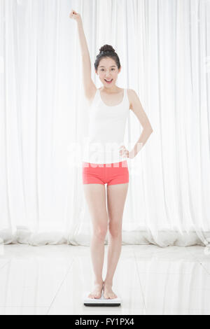 Young smiling woman standing on a scale holding a hand with one hand on her waist Stock Photo