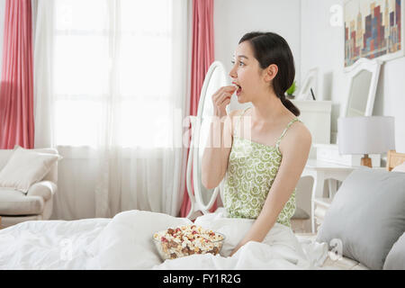Side view of young woman eating popcorn sitting in bed Stock Photo