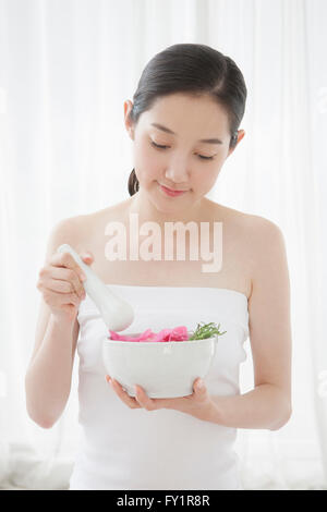 Young smiling woman holding herb and petals in mortar and medicine pestle looking down Stock Photo
