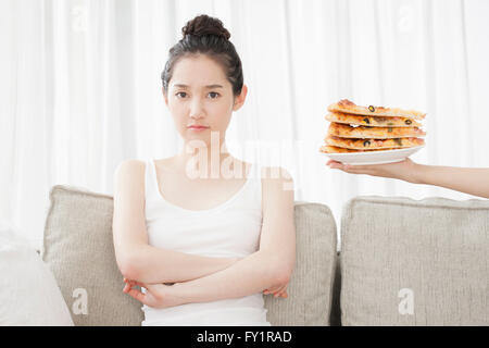 Portrait of young woman folding arms turning her face away from stacked pizza on plate Stock Photo