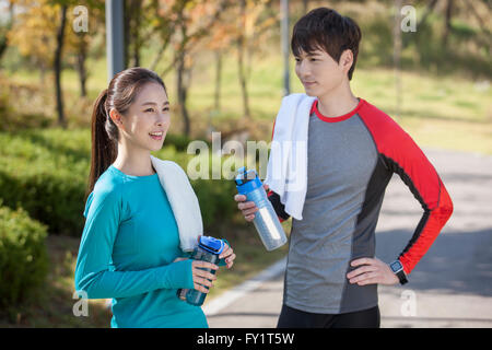 Side view of young smiling couple with water bottles and towels at park Stock Photo