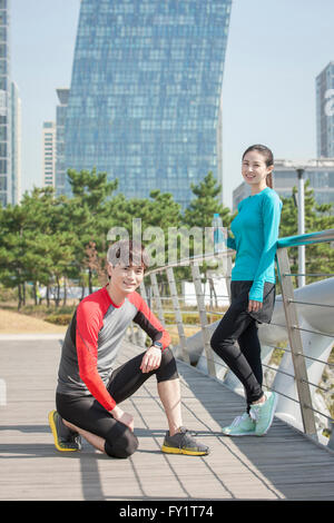 Side view of young smiling man sitting and young smiling woman standing staring at front Stock Photo