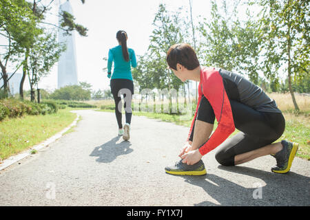 Back appearance of a jogging woman and a man tying his shoelace at the park Stock Photo
