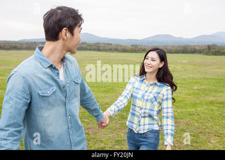 Man pulling a hand of his girlfriend at green field Stock Photo