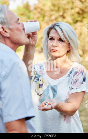 Woman helps old man to take his medicine and he drinks water Stock Photo