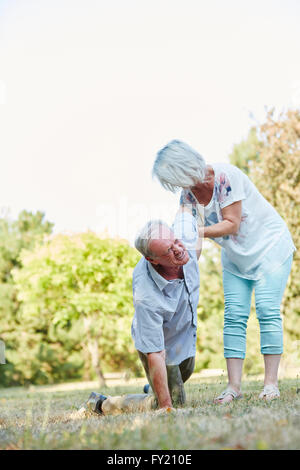 Senior woman helps man on his knees having a lumbago pain attack in the park in summer Stock Photo