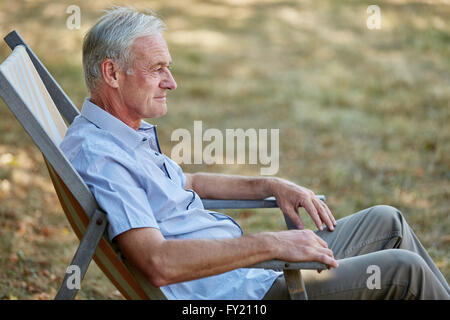 Old man sitting relaxed on a deck chair in summer in the nature Stock Photo