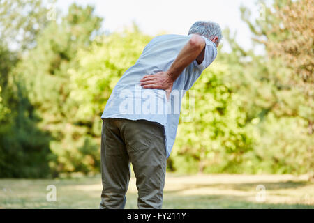 Old man with back pain while walking in the nature Stock Photo