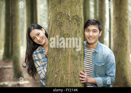 Couple hiding behind a tree and smiling Stock Photo