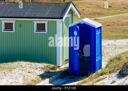 Falsterbo, Sweden - April 11, 2016: Blue rental toilet with an open door and no one inside. Toilet stand beside a green shack on Stock Photo