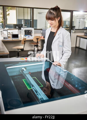 Female technician, 20-25 years, with a white lab coat, using a laser cutter in an electronics laboratory, Wattens Stock Photo