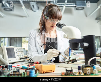 Female technician, 20-25 years, with a white lab coat, soldering a circuit board in an electronics laboratory, Wattens Stock Photo